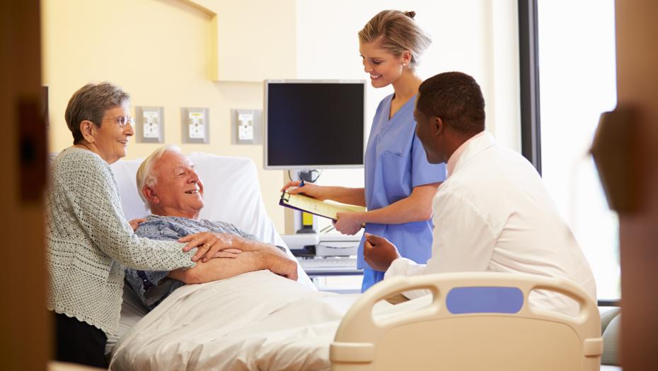 Wife and doctors around an old man laying in a hospital bed. It looks like the docs have good news, for they're smiling.