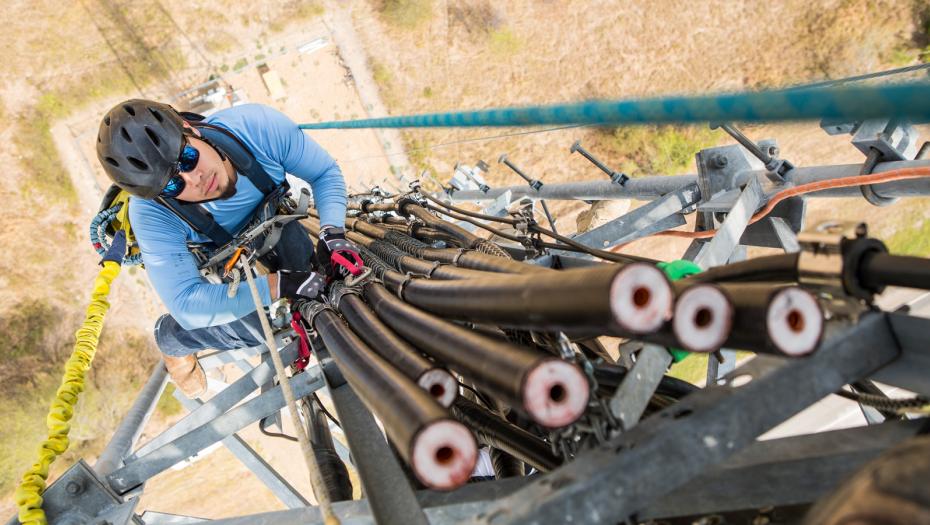 A man at the top of an electricity tower installing some new cables.